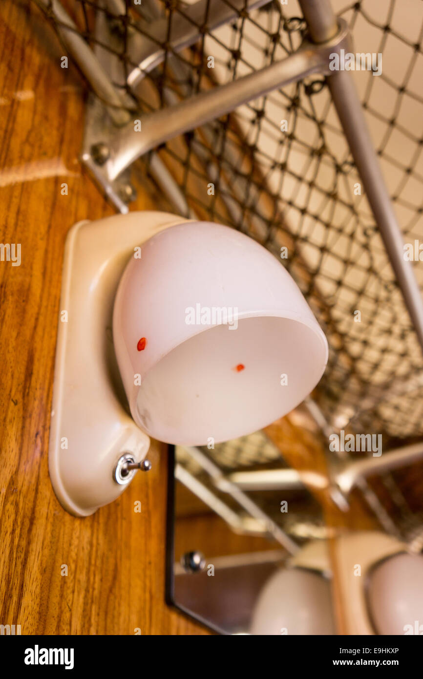 Vintage-Kabinenleuchte mit mattiertem Kuppelschirm und Wandschalter, montiert neben Gepäcknetz in einem alten Zug oder Transportwagen Stockfoto
