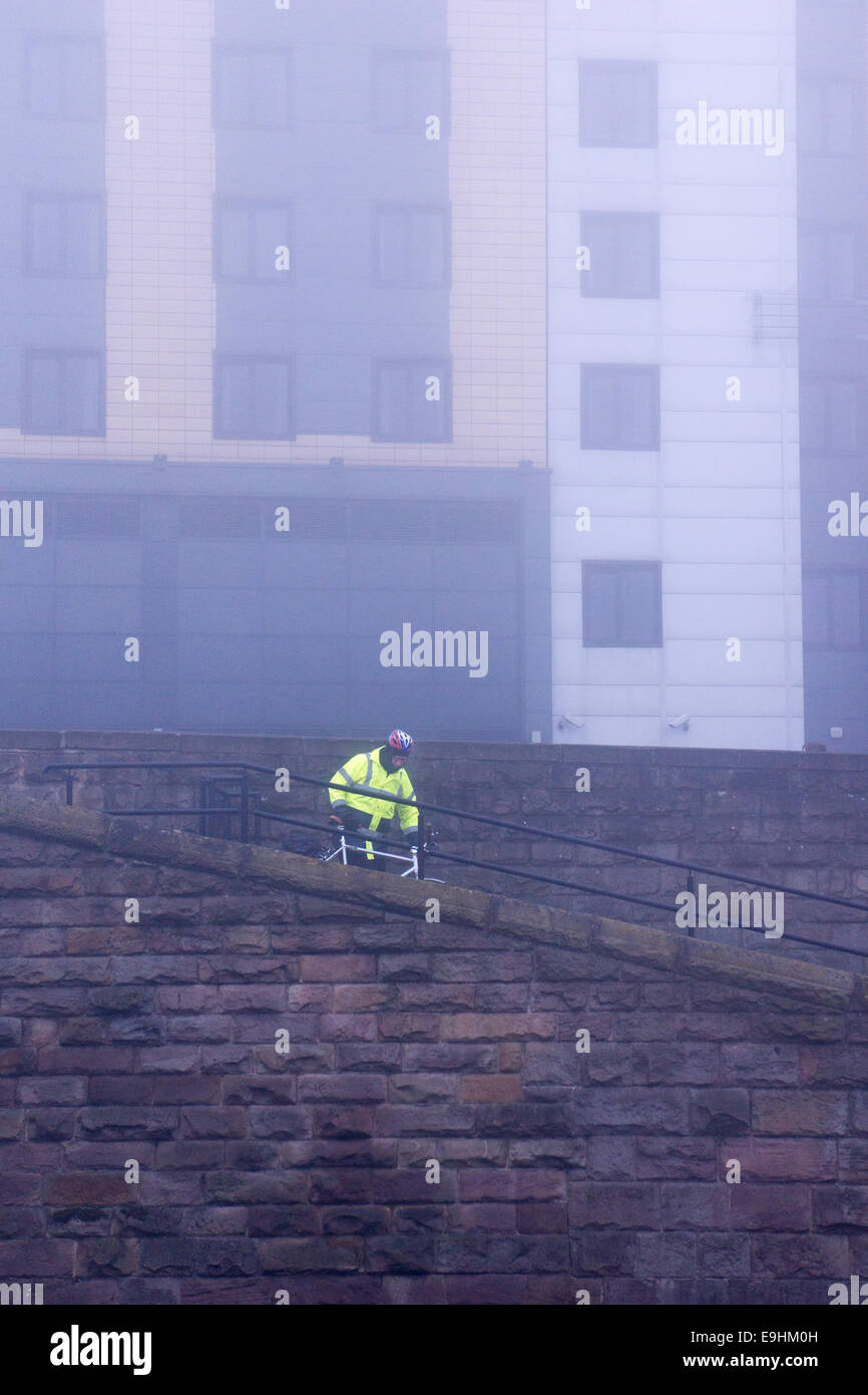 Arbeiter in gut sichtbarer Kleidung, der an einer Steinmauer im nebligen Nottingham entlang geht, mit modernen Gebäuden, die in den Nebel fallen Stockfoto