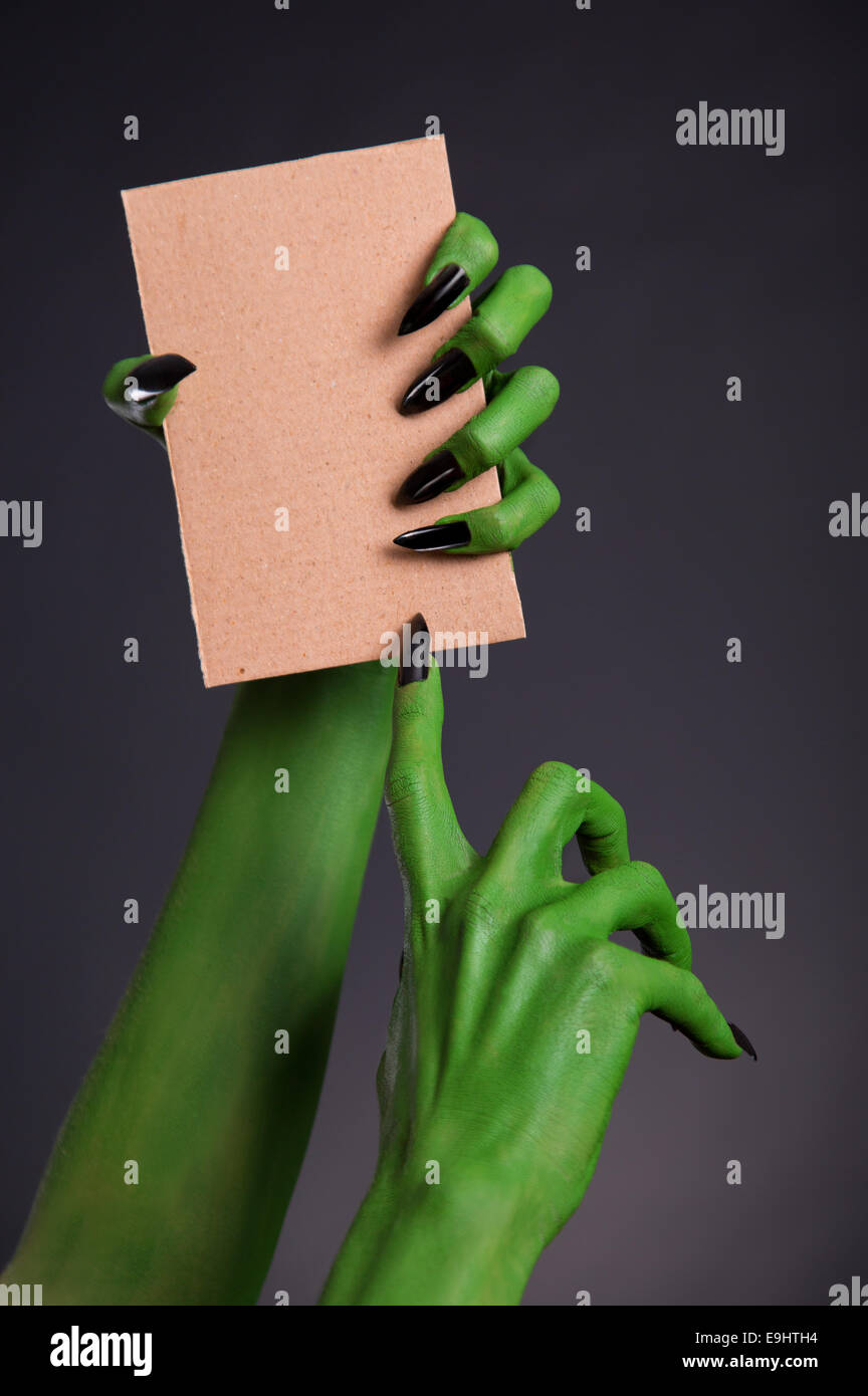 Grünes Monster Hände mit schwarzen Nägeln halten leeres Blatt Karton, Halloween-Thema Stockfoto