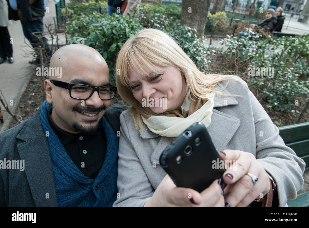 Eine authentische Paare sitzen auf einer Bank in Paris und eine selfie auf einem Smartphone während der Happy suchen Stockfoto