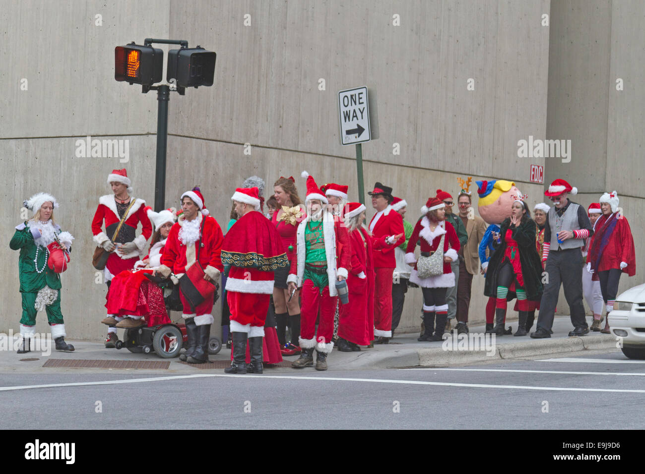 Eine Packung Weihnachtsmänner, Frau. Klauseln und Elfen warten eine Straße in der Innenstadt von Asheville um Weihnachten während der Veranstaltung zu überqueren, santacon Stockfoto
