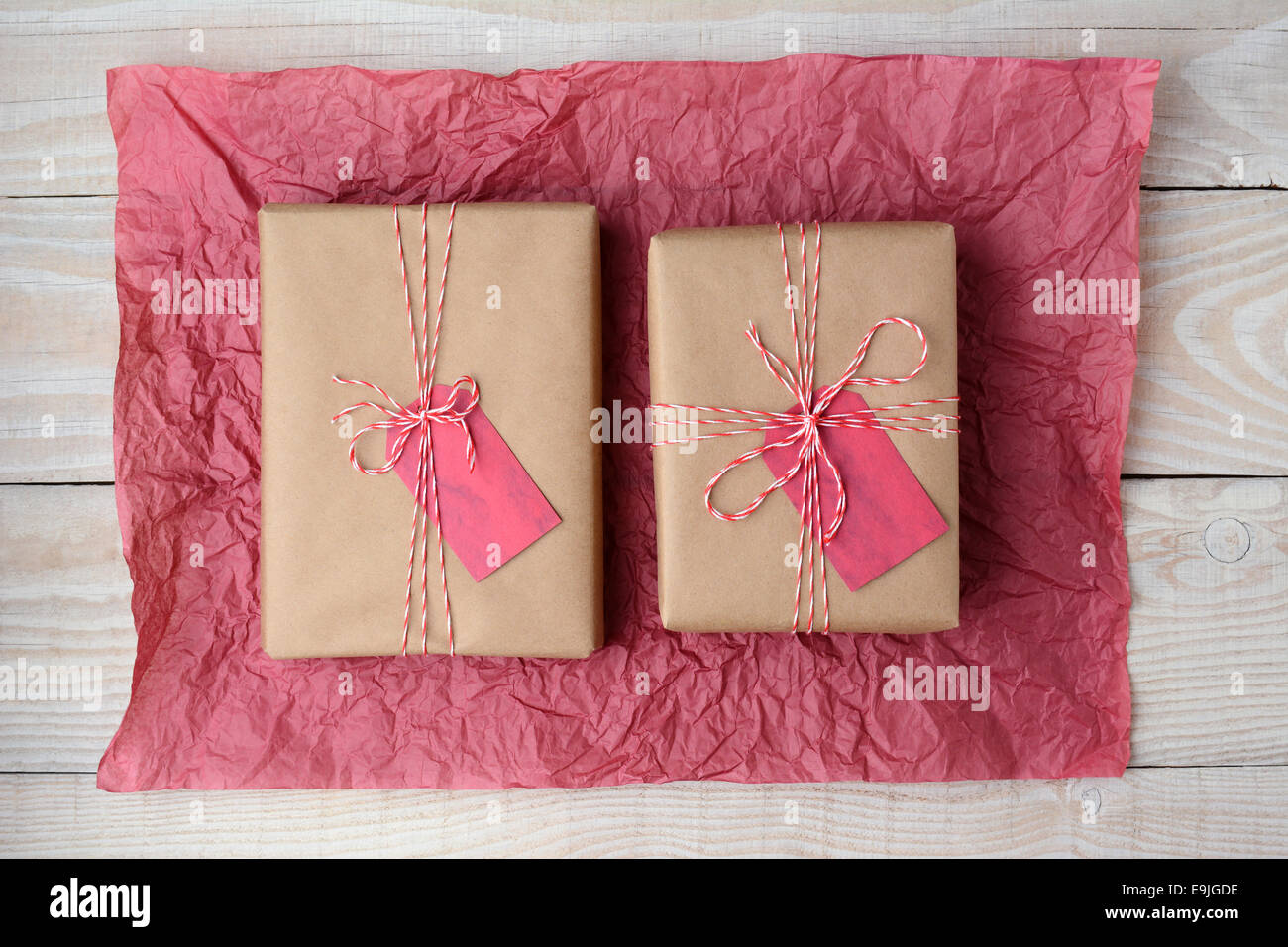 Hohen Winkel Schuss von zwei braunen Papier eingewickelt präsentiert auf ein zerknittertes Blatt rot Tissue-Papier. Querformat Stockfoto