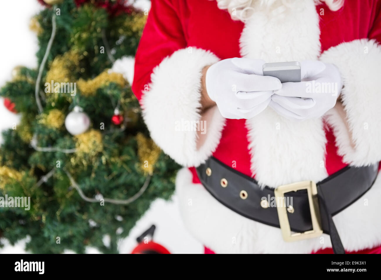 Santa mit Smartphone mit Weihnachtsbaum hinter ihm Stockfoto