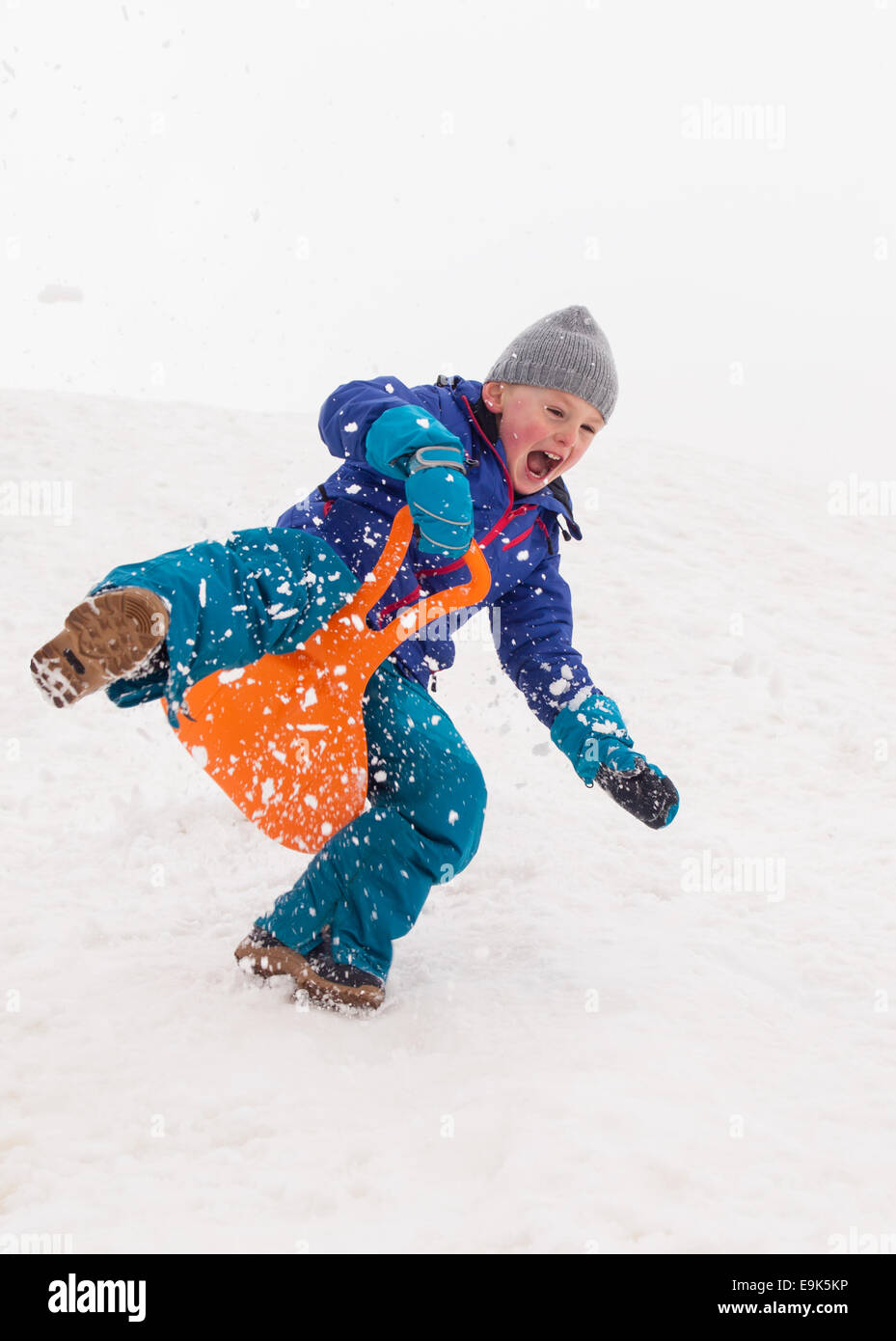 kleinen lachenden jungen schnell hinunter einen steilen Hügel in einer Wolke aus Schnee Rodeln Stockfoto