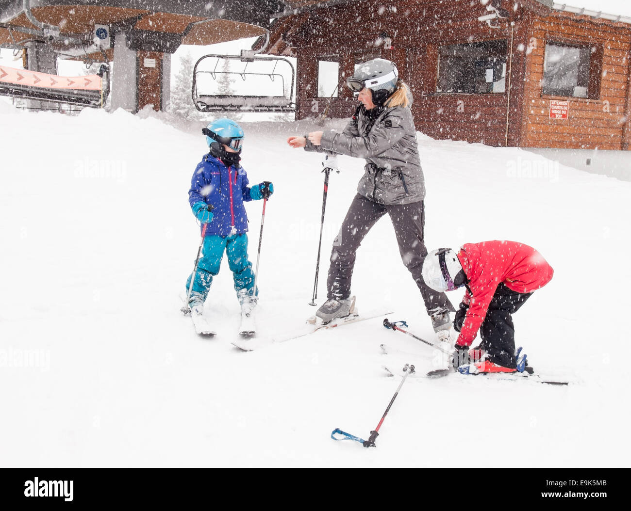 Frau hilft kleine Kindern bereiten vor ein Skilift in schweren fallenden Schnee Skifahren Stockfoto