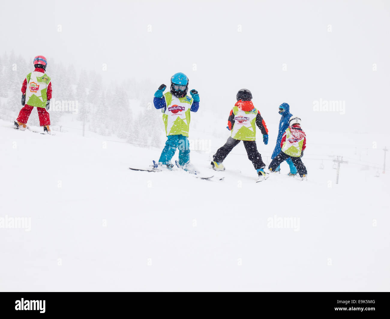 Kleinkinder im Alter von fünf Jahren tragen Helme und Brillen in einem Gruppenkurs mit Instruktor in fallenden Schnee Skifahren lernen Stockfoto