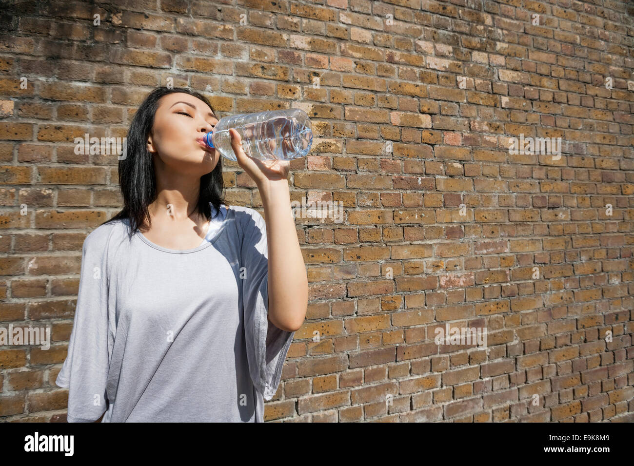 Schöne junge Frau Trinkwasser gegen Mauer Stockfoto