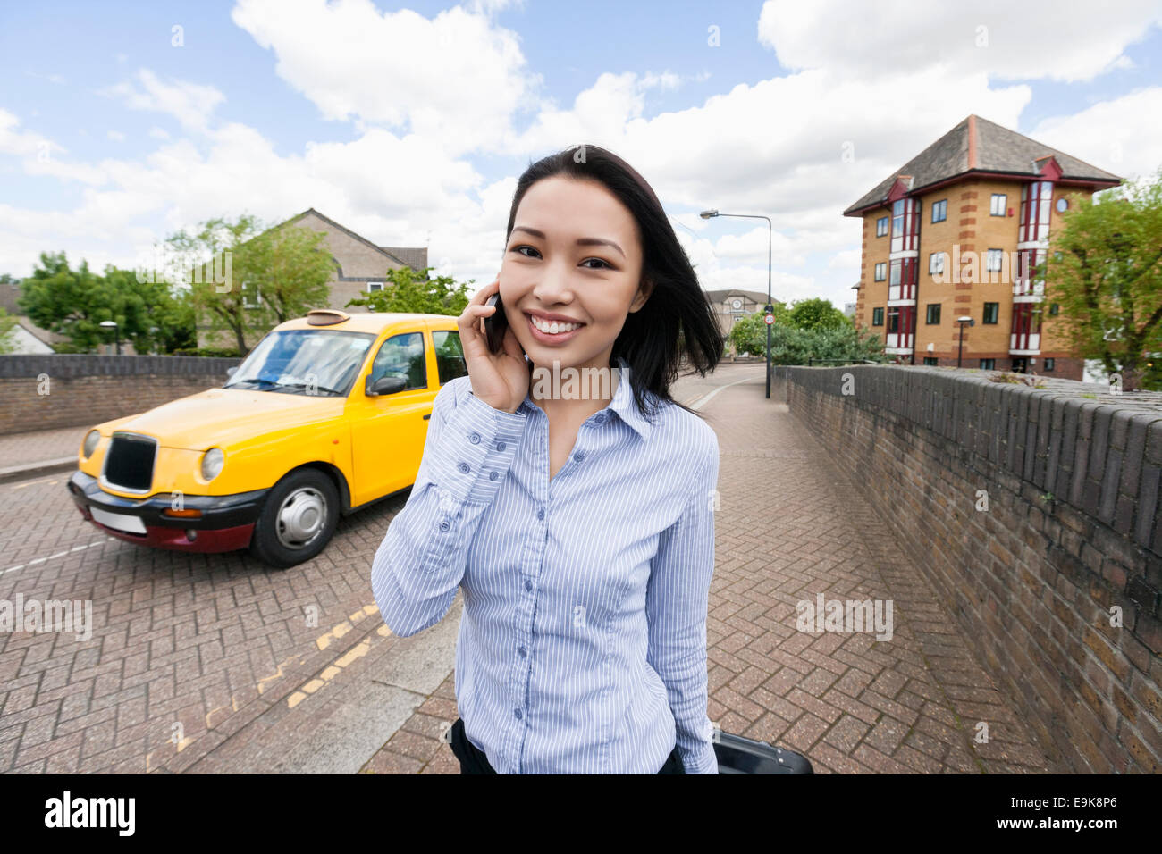 Porträt des Lächelns Geschäftsfrau Beantwortung Handy auf Bürgersteig mit Taxi im Hintergrund Stockfoto