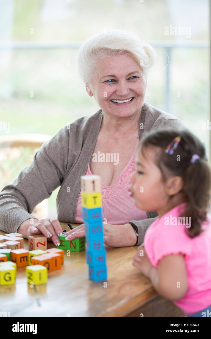 Glückliche Großmutter wegschauen während Enkelin bläst Alphabet Block im Haus gestapelt Stockfoto