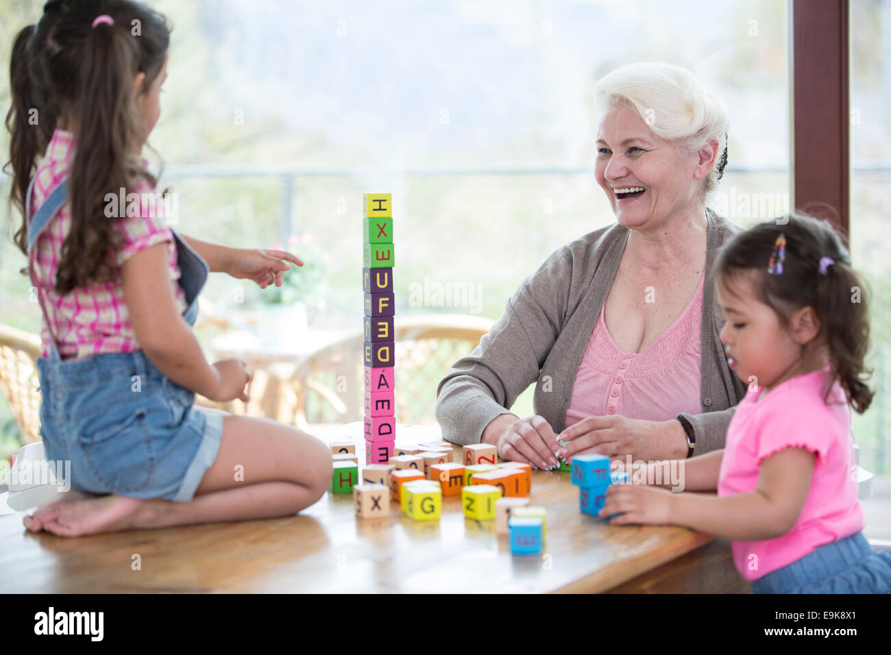 Glückliche Großmutter und Enkelinnen mit Alphabet Blöcke am Tisch spielen Stockfoto