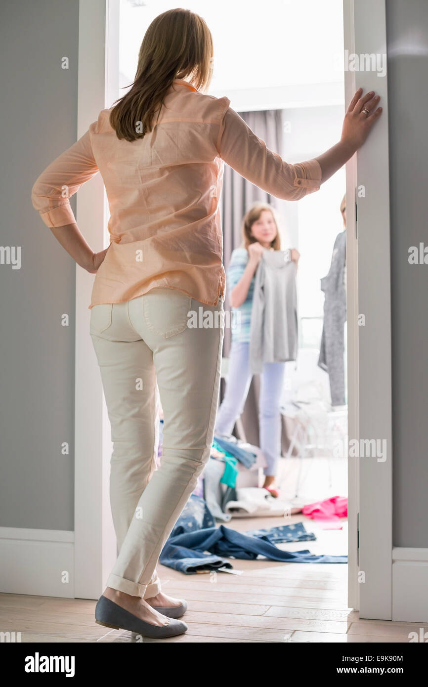 Full-length Rückansicht der Mutter beobachtete Töchter versuchen auf Kleidung im Zimmer Stockfoto