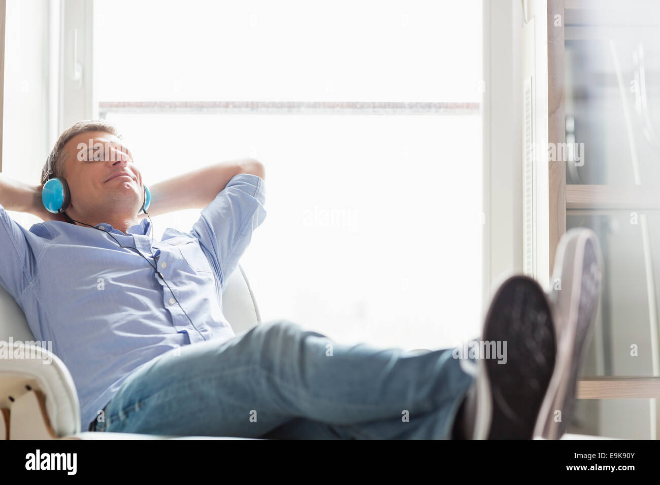 Der entspannte Mann mittleren Alters Musikhören zu Hause in voller Länge Stockfoto