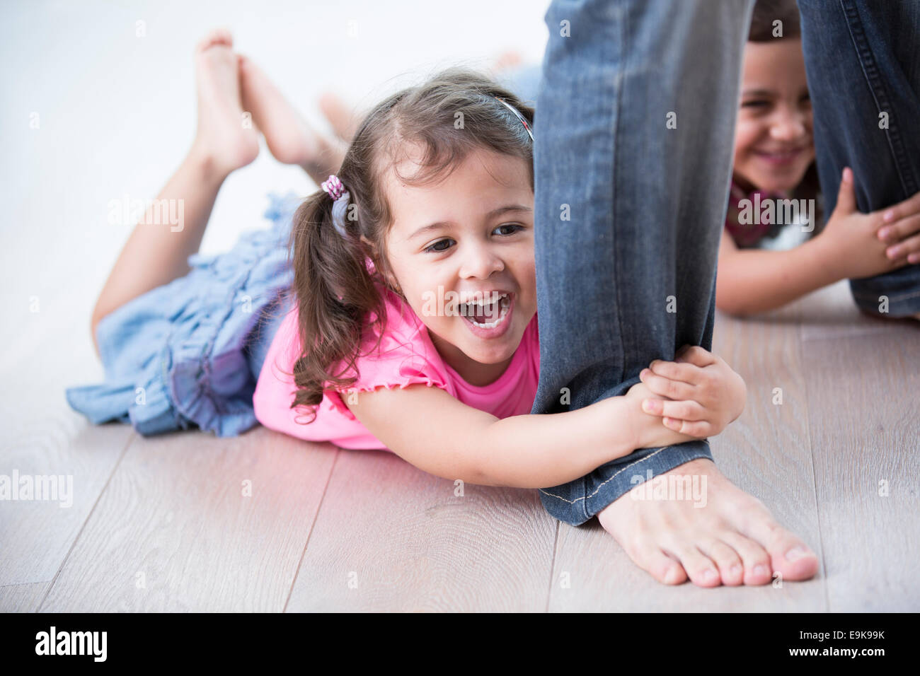 Verspielte Mädchen Hartholz-Fußboden des Vaters Beine festhalten Stockfoto