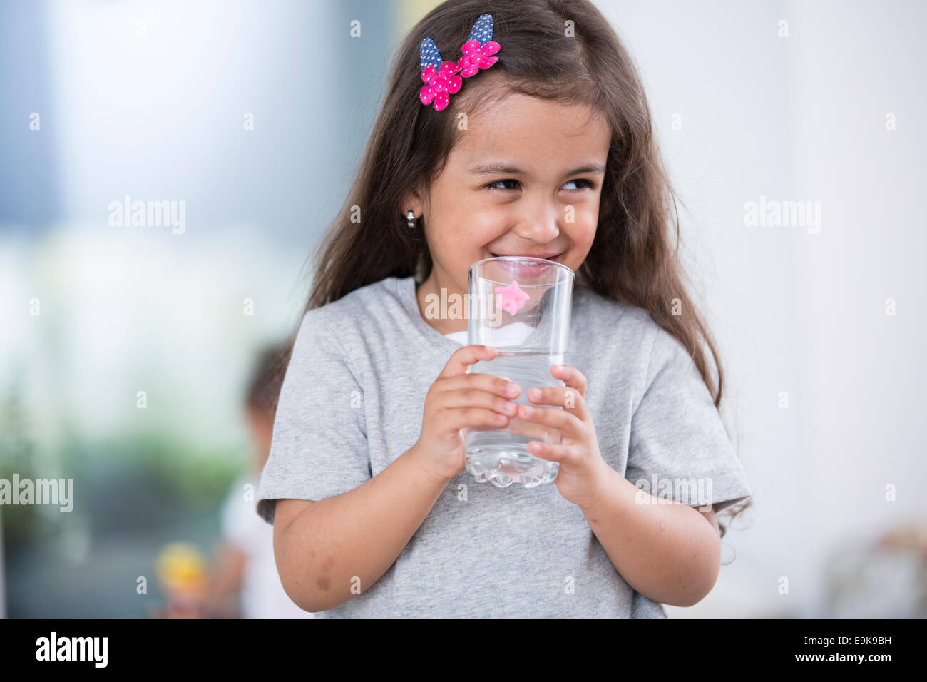 Lächelnde niedliche Mädchen hält Glas Wasser zu Hause Stockfoto