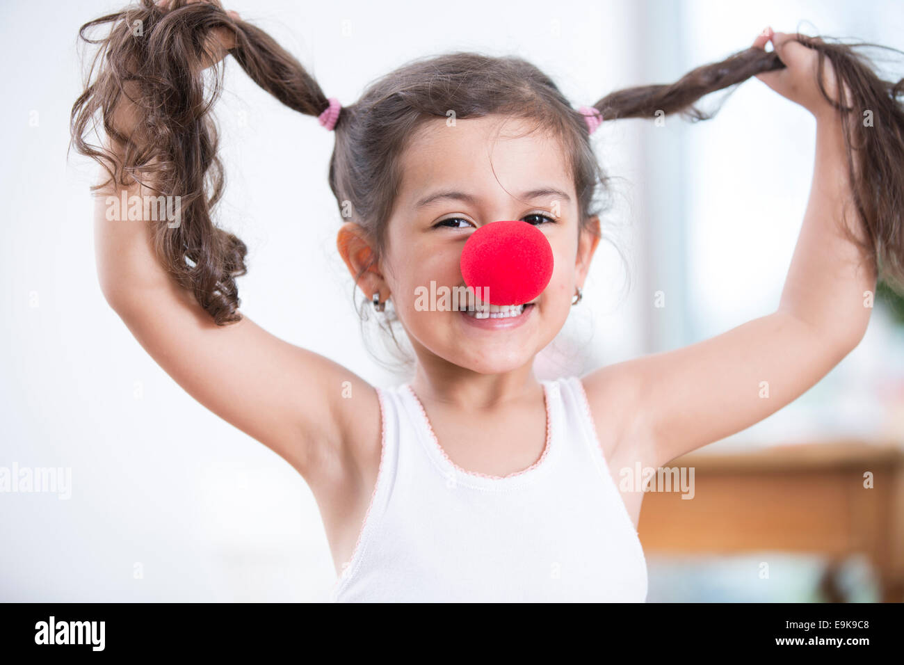 Porträt der verspielte kleine Mädchen tragen Clownsnase Zöpfen zu Hause halten Stockfoto