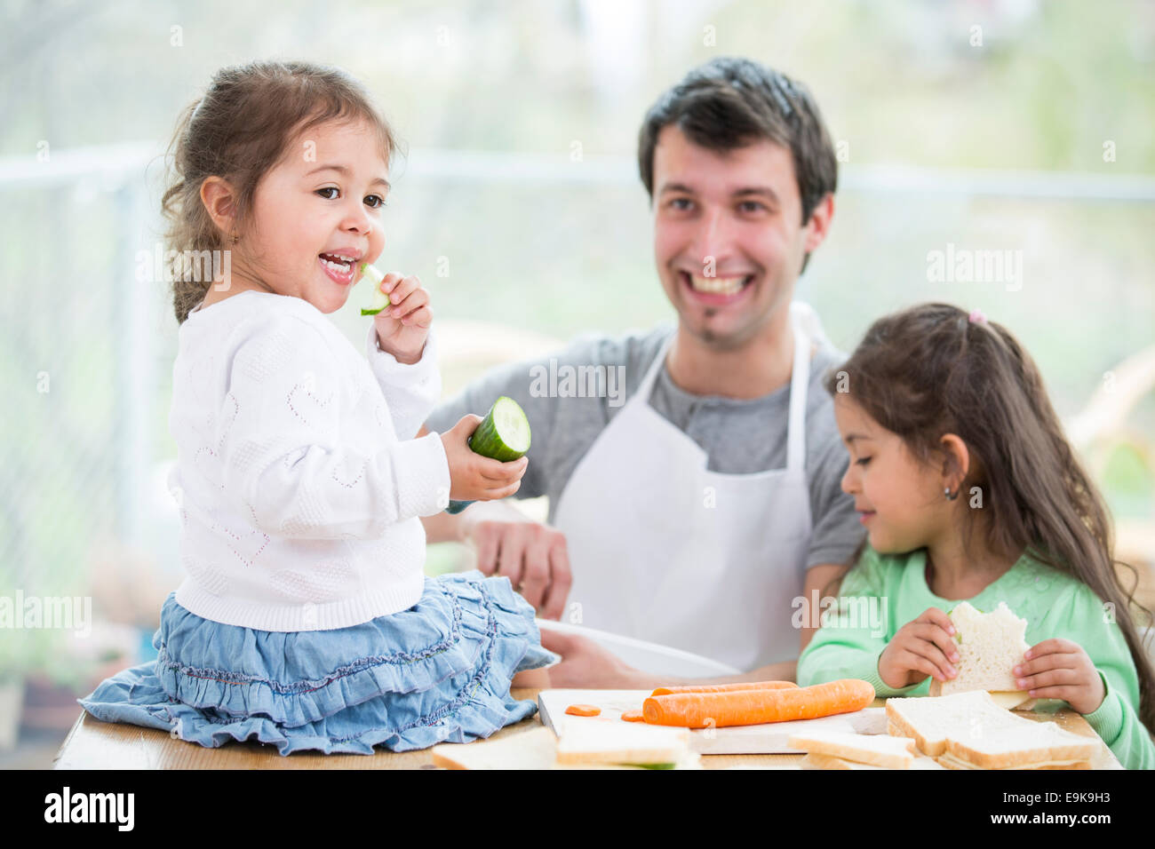 Glücklicher Vater Vorbereitung Sandwiches während der Töchter zu Hause essen Stockfoto
