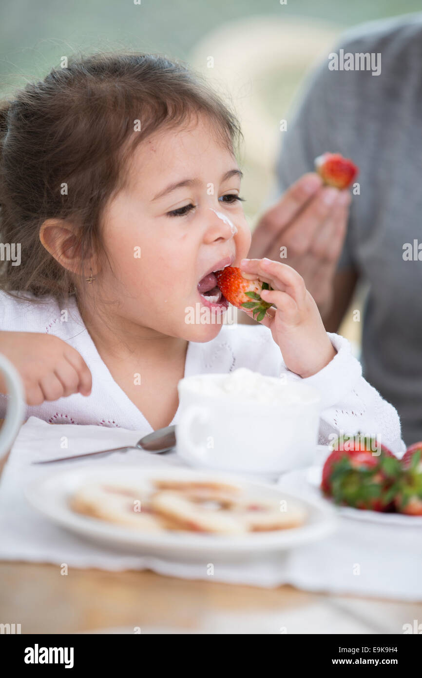 Niedliche kleine Mädchen essen Erdbeeren mit Vater am Frühstückstisch Stockfoto