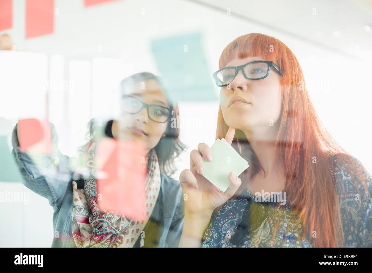 Geschäftsfrauen Haftnotizen auf Glaswand in Kreativbüro lesen Stockfoto