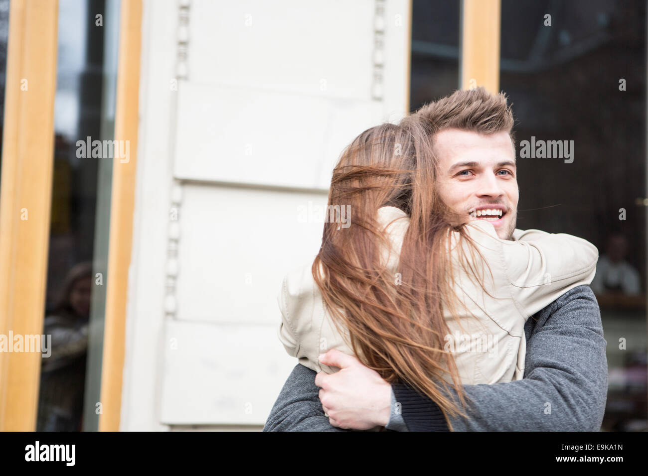 Glücklicher junger Mann umarmt Frau vor café Stockfoto
