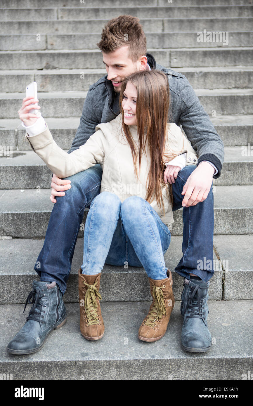 Volle Länge des jungen Paares unter Bild von sich selbst auf Schritte im freien sitzend Stockfoto
