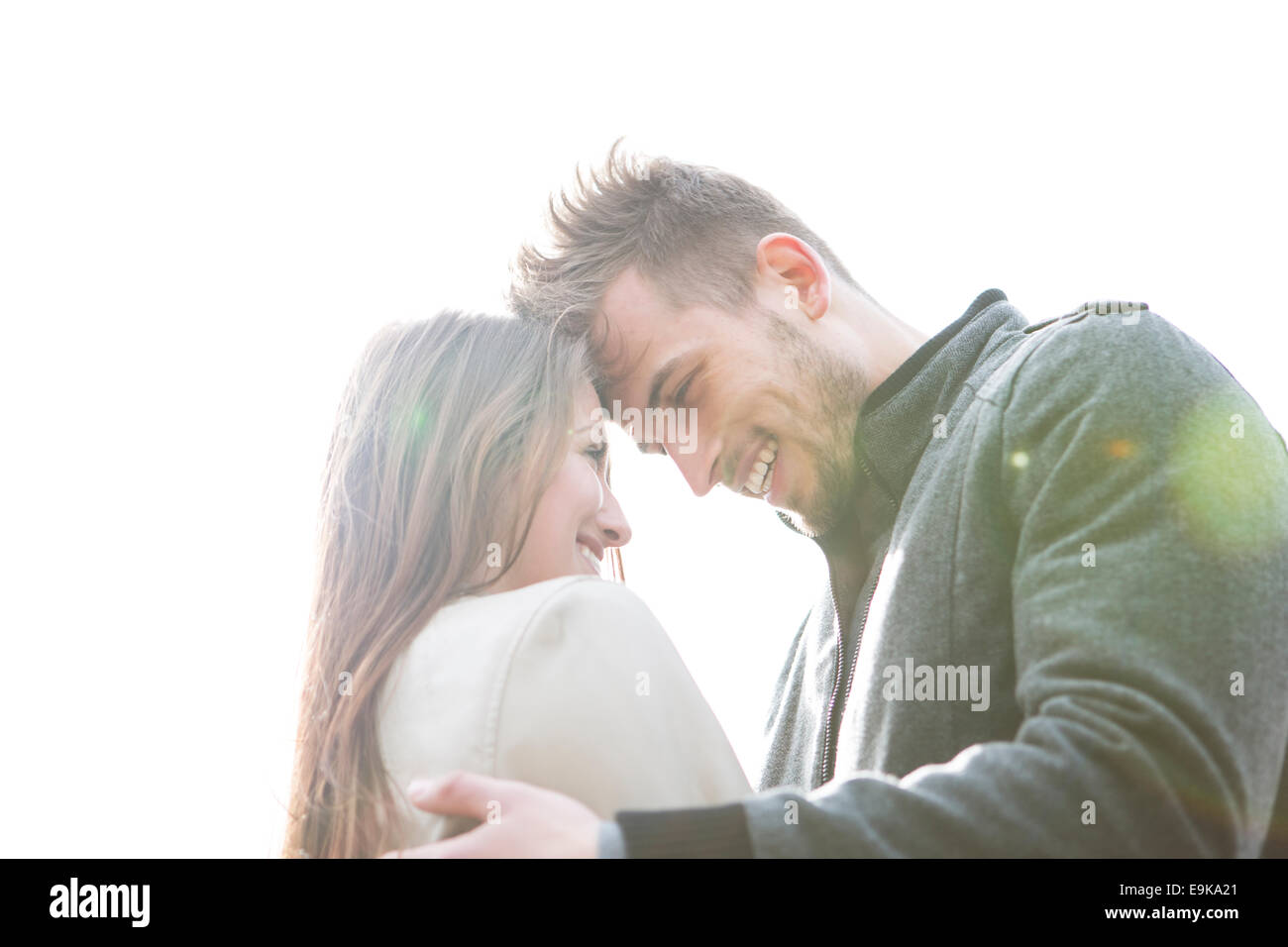 Lächelnd junger Mann und Frau gegen klaren Himmel umarmen Stockfoto