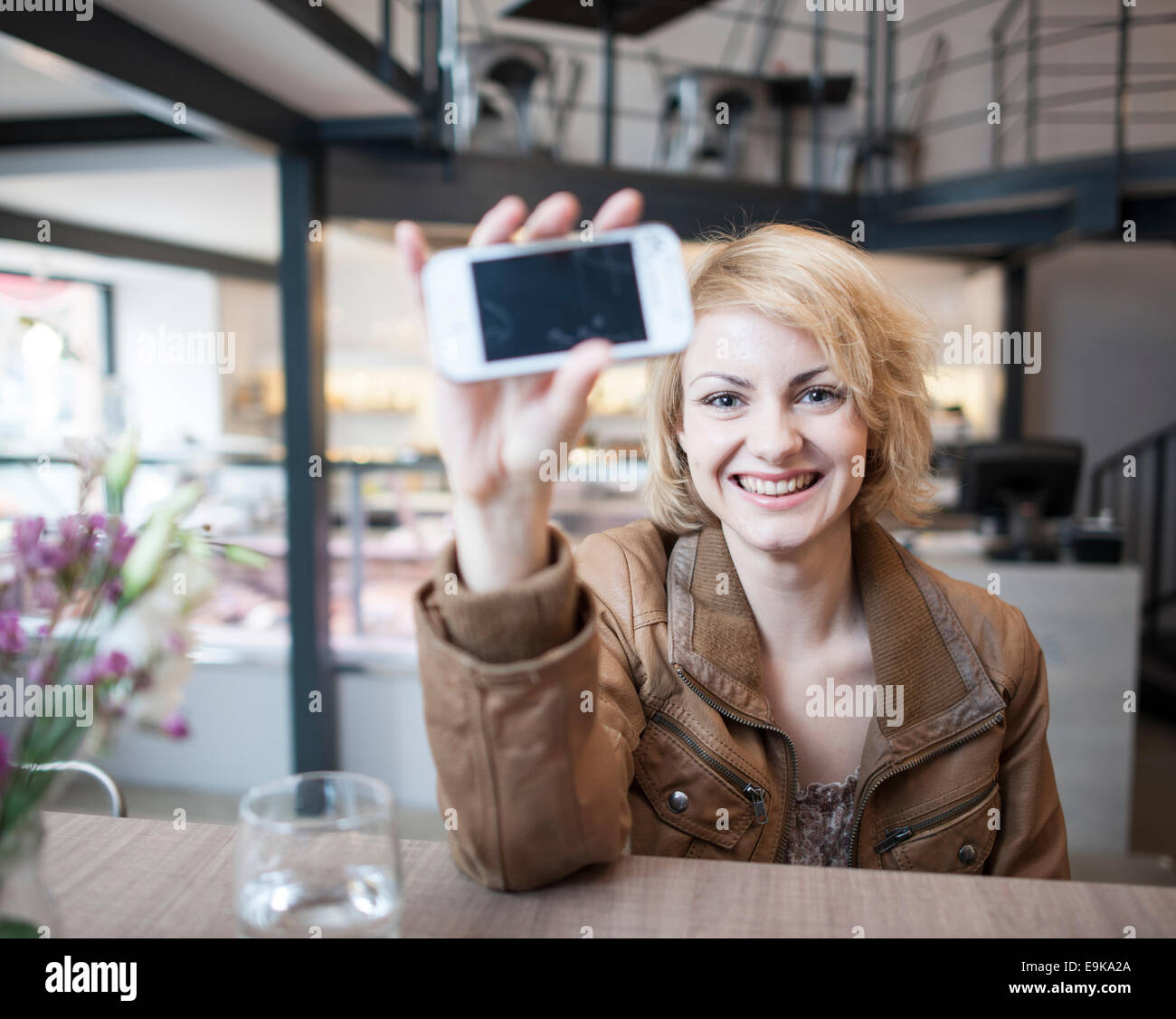 Porträt der lächelnde junge Frau in Café Handy anzeigen Stockfoto