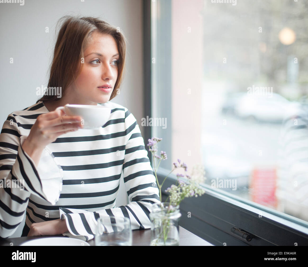 Nachdenkliche junge Frau mit Blick vom Fenster beim Kaffeetrinken im café Stockfoto