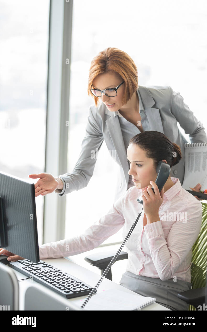 Geschäftsfrau mit Festnetz-Telefon während Manager in Richtung Computer im Büro Stockfoto