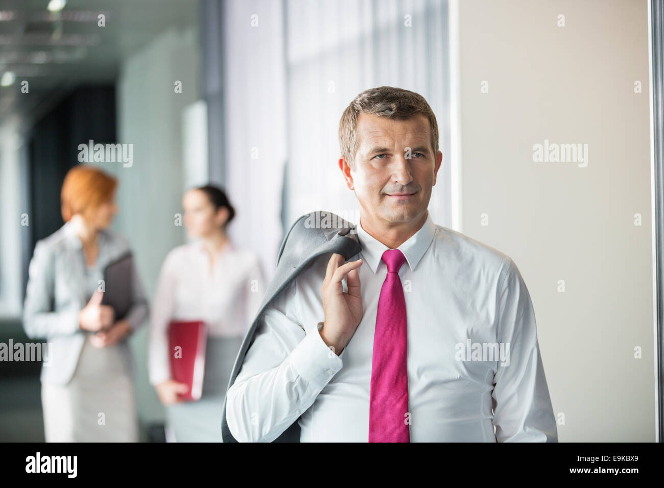 Geschäftsmann Holding Mantel über die Schulter mit Kolleginnen im Hintergrund im Büro Stockfoto
