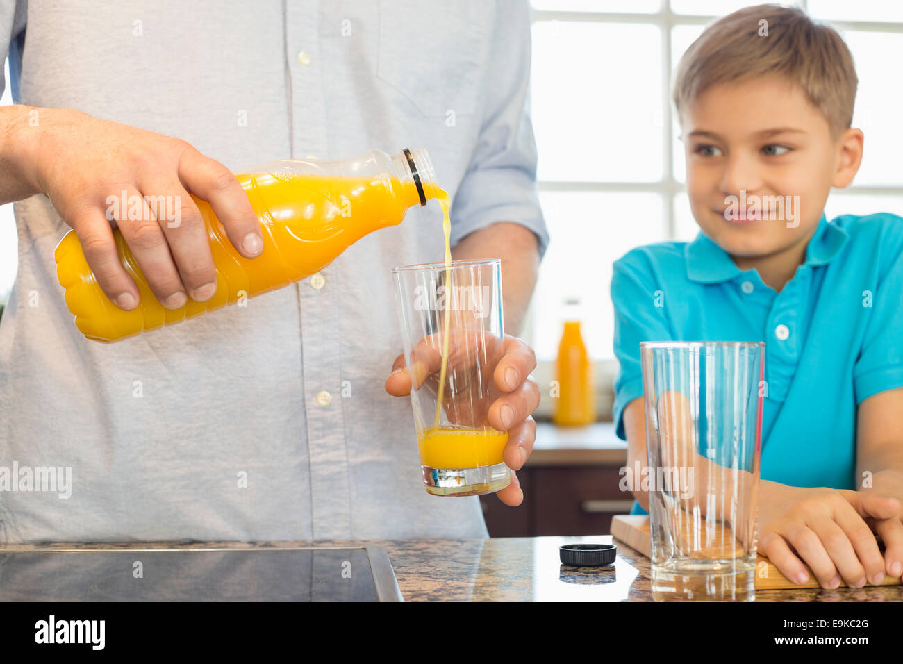 Mittelteil des Vaters servieren Orangensaft für Sohn in Küche Stockfoto