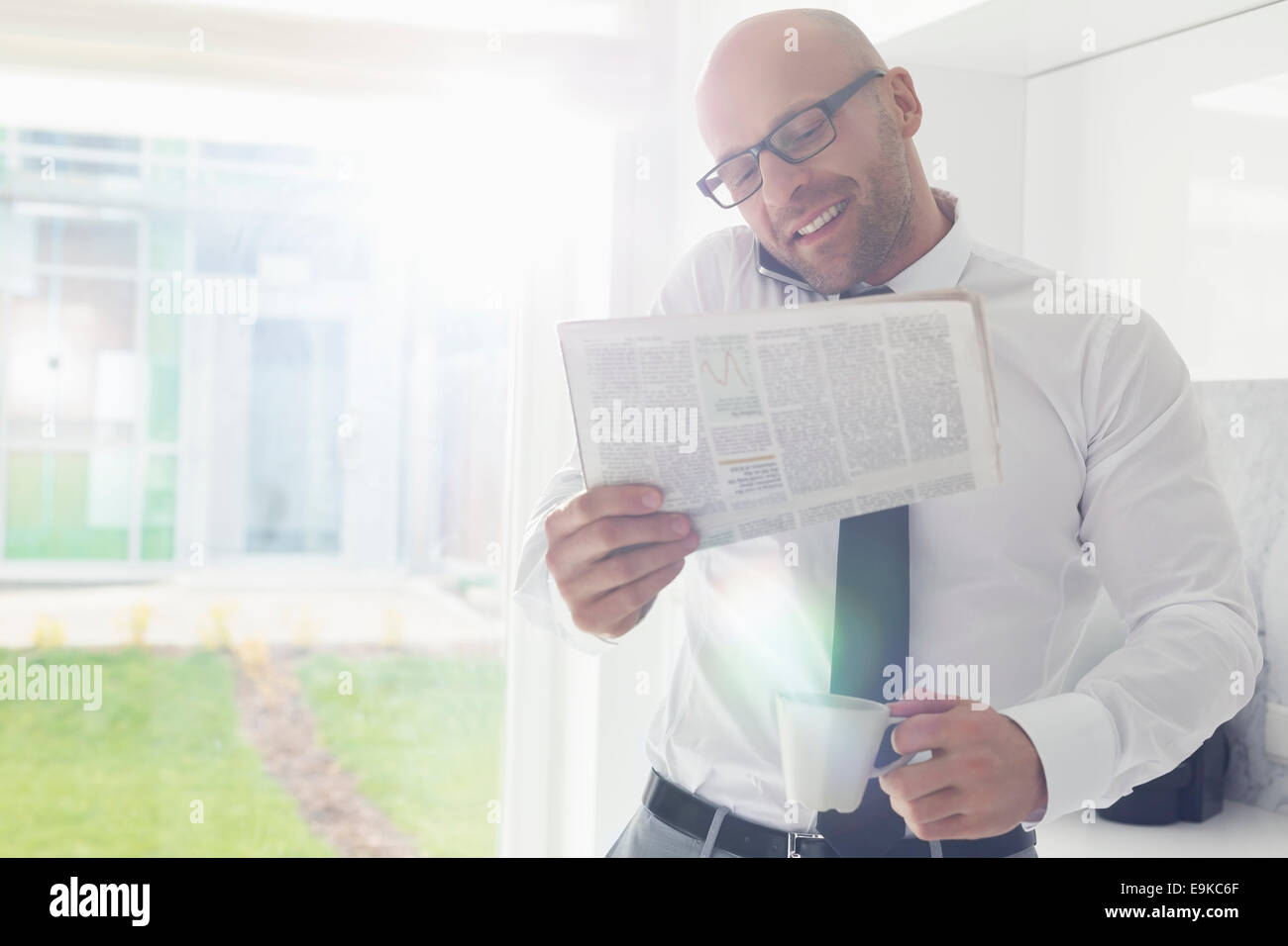 Mitte adult Geschäftsmann auf Abruf halten Sie Zeitung und Kaffeetasse zu Hause Stockfoto