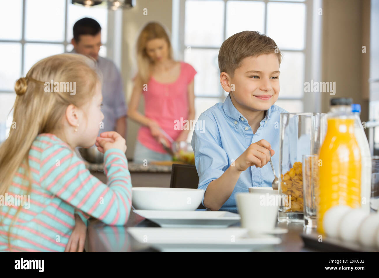Geschwister mit Frühstück am Tisch mit Eltern kochen im Hintergrund Stockfoto