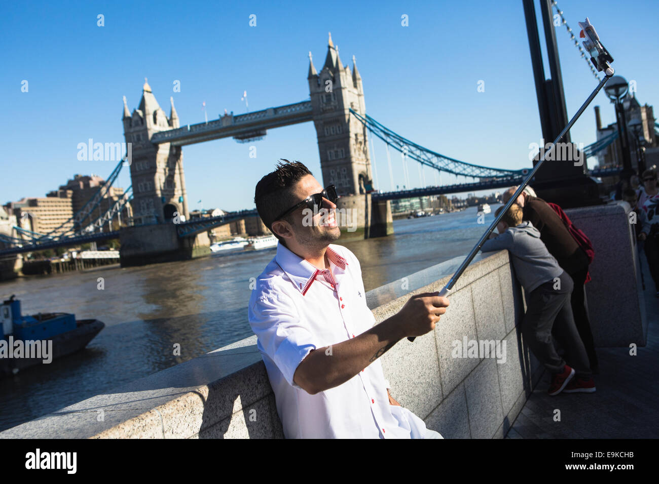 Ein Mann nimmt ein Bild von sich selbst neben Tower Bridge mit einem Selfie-Stick an der Themse in London Stockfoto