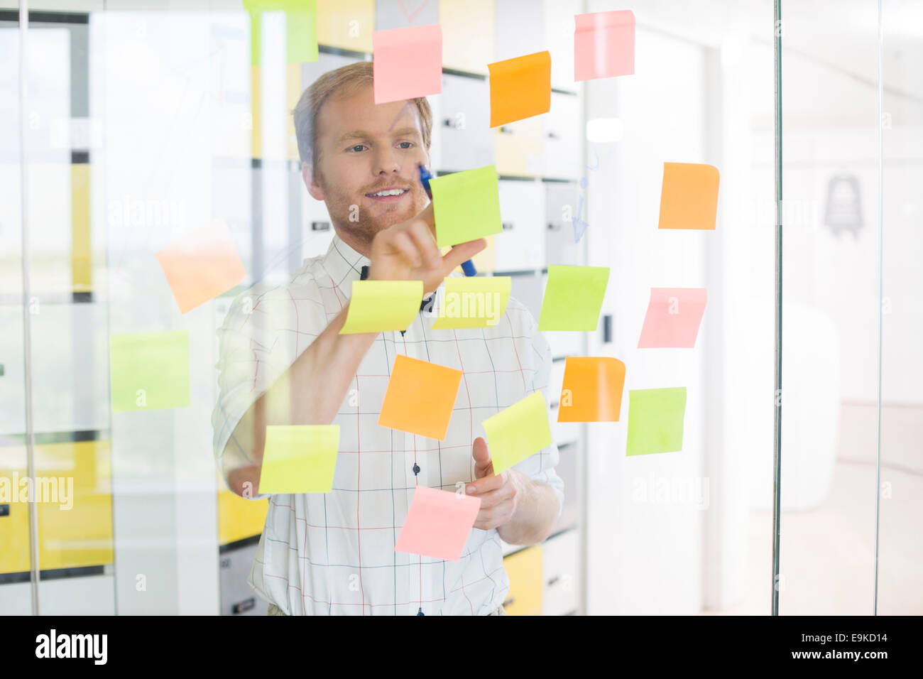 Junger Geschäftsmann klebrigen Papier an Glaswand an Kreativbüro lesen Stockfoto