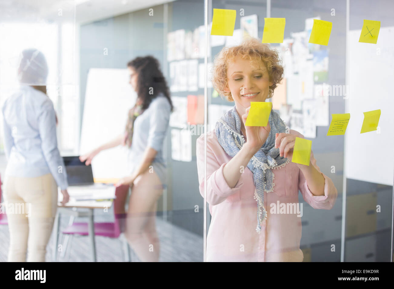 Geschäftsfrau Haftnotizen auf Glas mit Kollegen im Hintergrund lesen Stockfoto