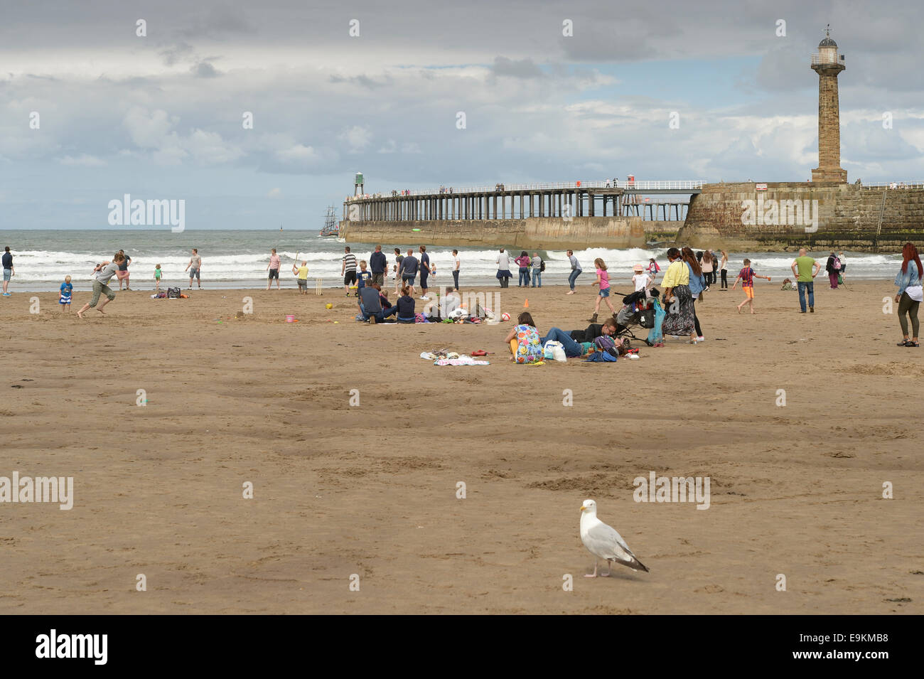 Urlauber am Strand auf einer bedeckt einen bewölkten Sommertag in der Nähe von Whitby Pier, N Yorks, UK. Stockfoto