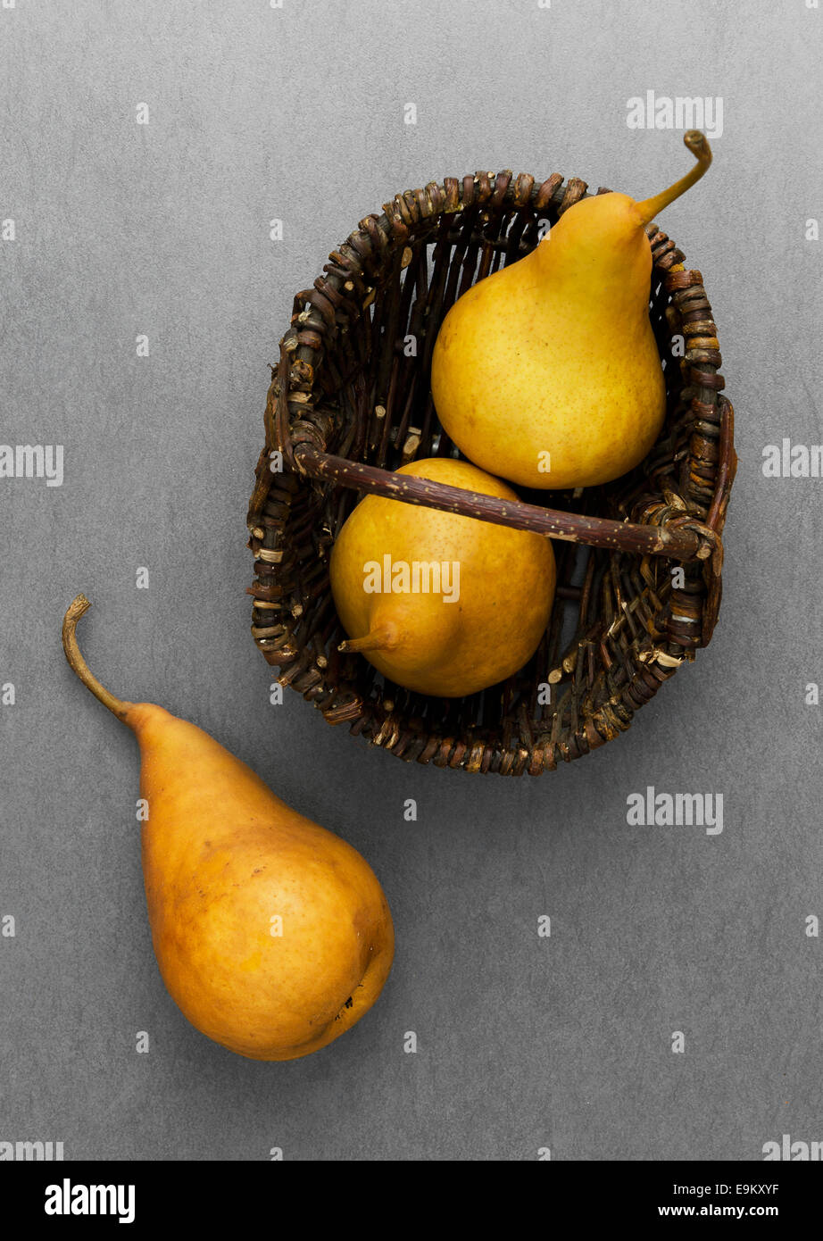Drei reife Birnen im rustikalen Korb über dunklen grauen Hintergrund Stockfoto