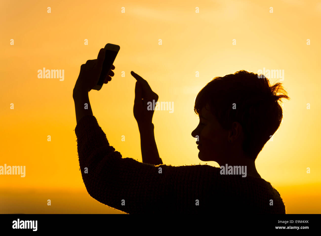 Eine Silhouette Mädchen nutzt ein Handy auf eine Roaming-Verpackung während des Urlaubs während des Sonnenuntergangs. Stockfoto