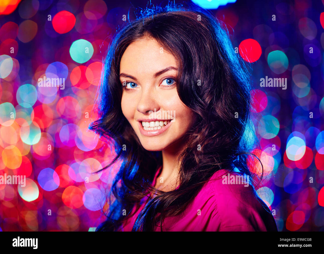 Porträt von schöne Brünette Blick in die Kamera mit toothy Lächeln über glitzernden Hintergrund Stockfoto