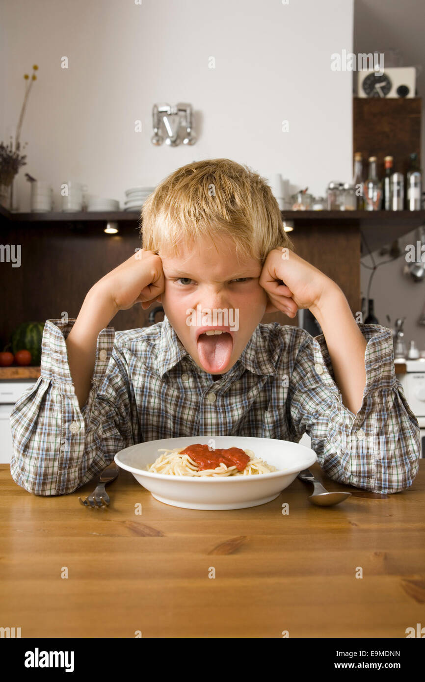 Junge sitzt vor Schüssel Spaghetti und Zunge heraus Stockfoto