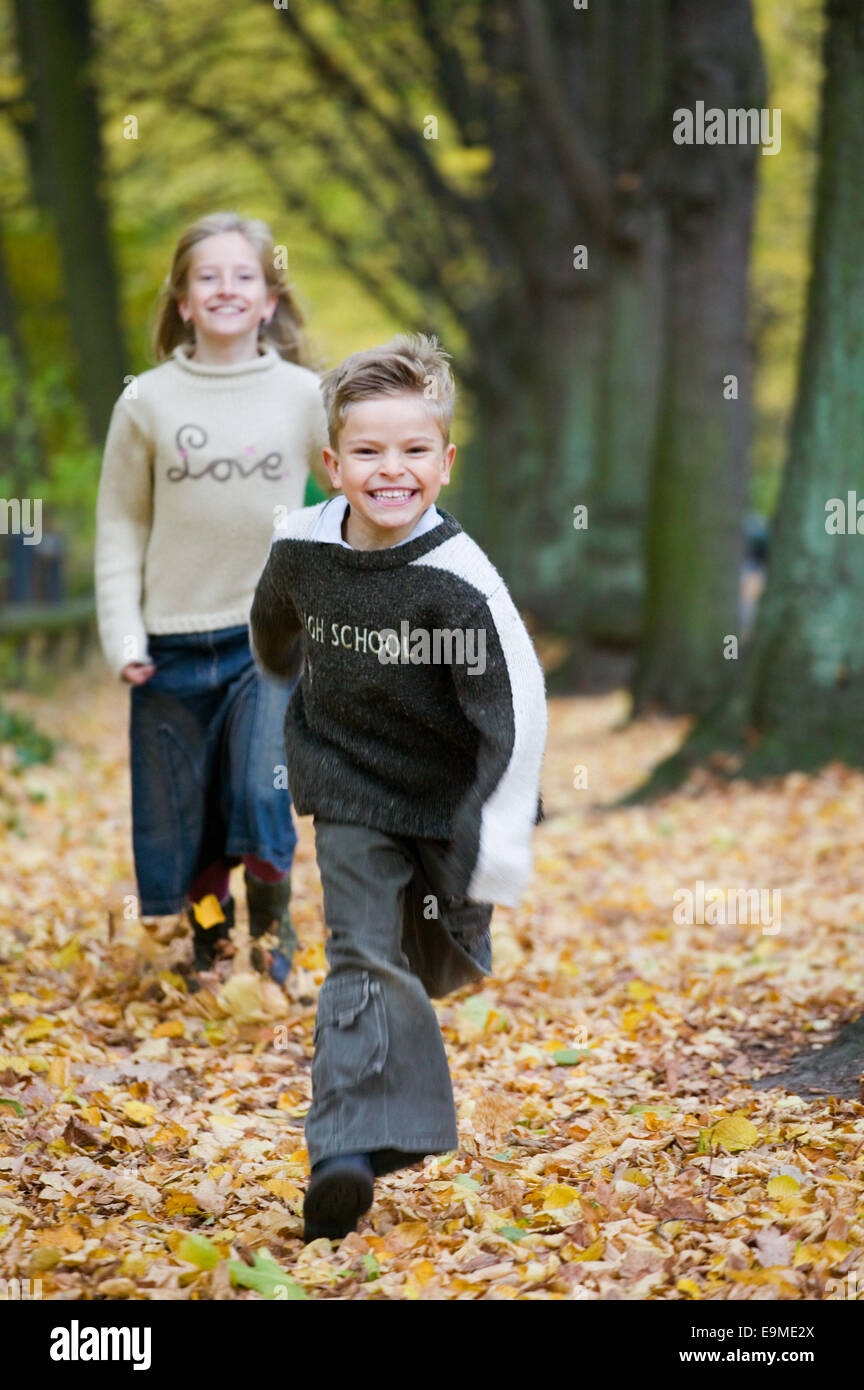 Junge läuft vor Mädchen Weg fallenden Herbst Blätter Stockfoto