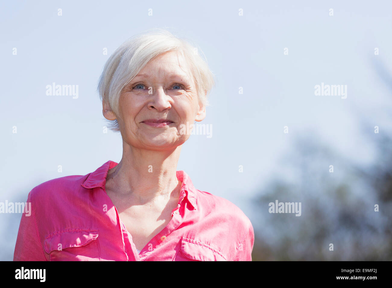 Reife Frau lächelnd während wegschauen gegen Himmel Stockfoto