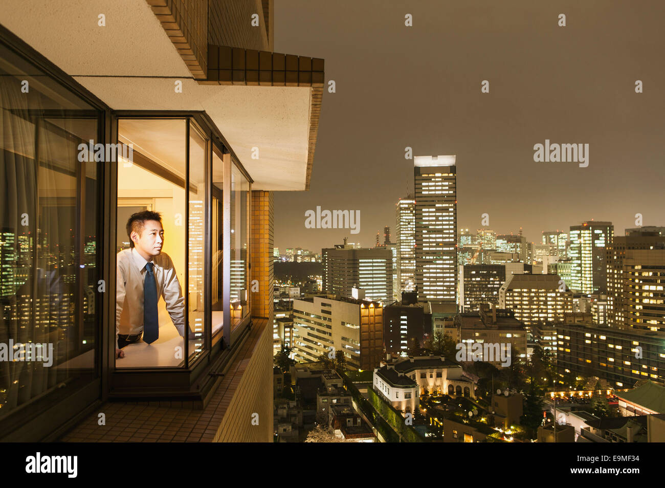 Geschäftsmann, Blick auf beleuchtete Stadtbild durch Fenster in der Abenddämmerung Stockfoto