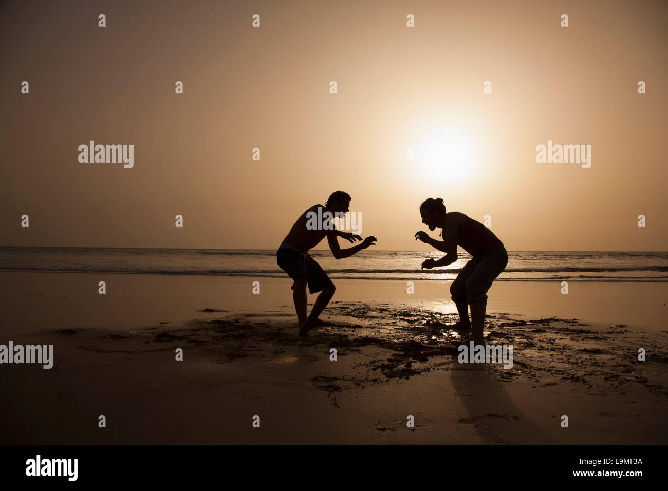 Voller Länge Silhouette männliche Freunde spielen am Strand bei Sonnenuntergang Stockfoto