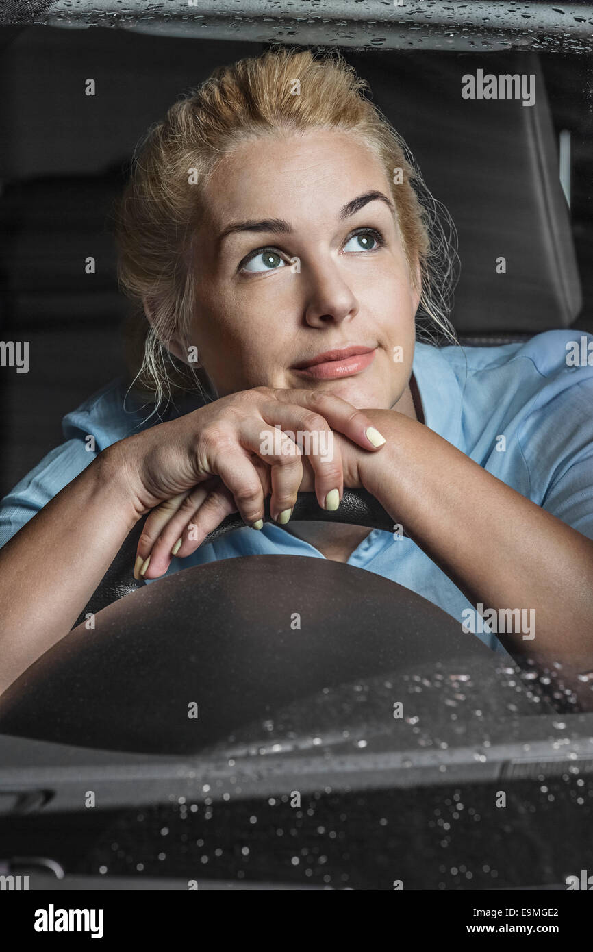 Nachdenkliche Frau lehnt sich am Lenkrad im Auto Stockfoto