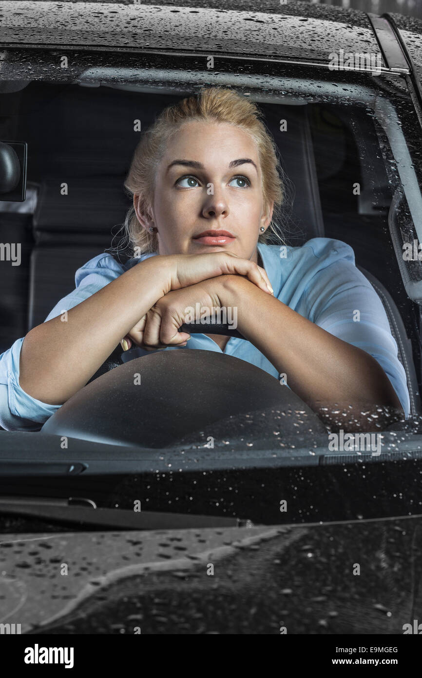 Nachdenkliche Frau entspannend am Lenkrad im Auto Stockfoto