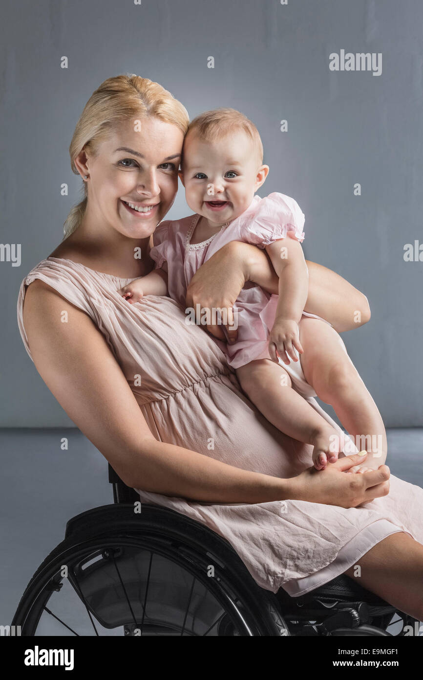 Porträt der glückliche Mutter mit Babymädchen im Rollstuhl gegen graue Wand Stockfoto