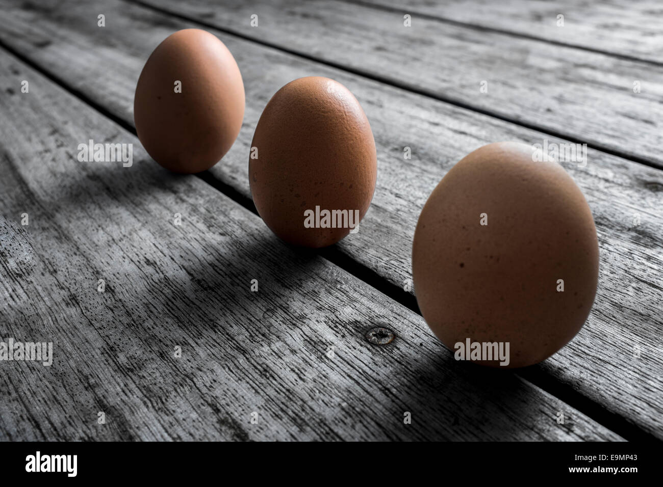 Drei kostenlose reichen Hühnereiern auf einem entsättigten hölzernen Hintergrund angeordnet. Stockfoto