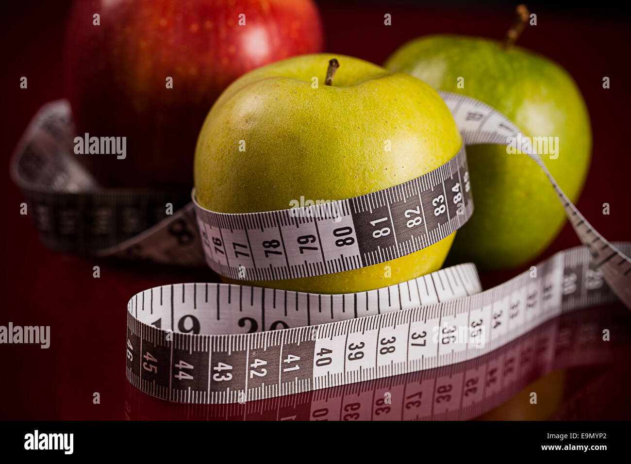 Äpfel mit Maßband auf rotem Grund Stockfoto
