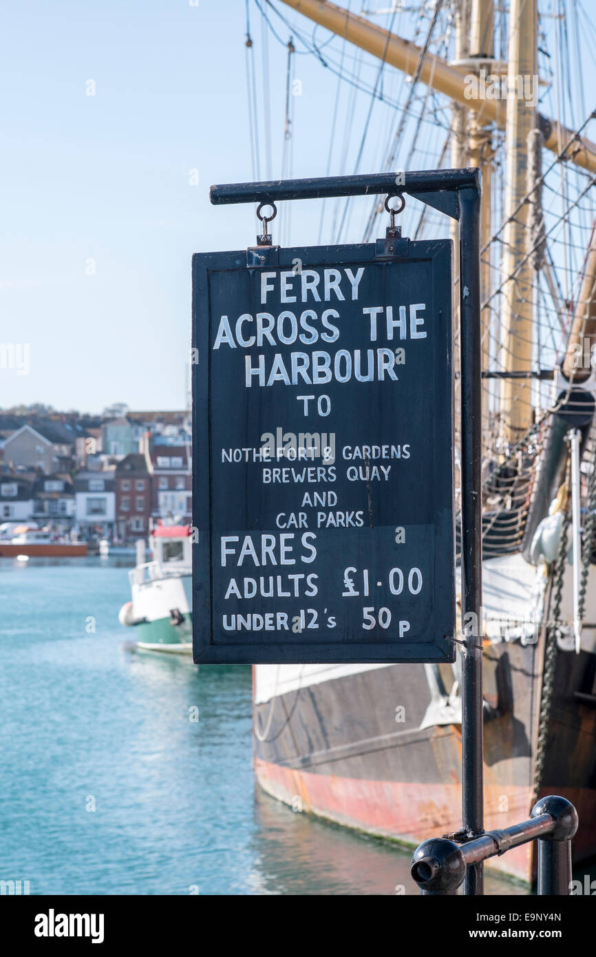Weymouth Hafen Fähre Werbung Tafel anzeigen Tarife Preise in weißer Schrift mit Hafen und Wasser im Hintergrund Stockfoto